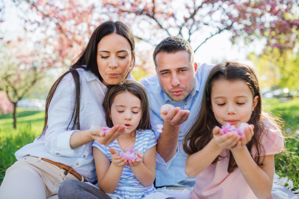 Front view of young parents with small daugthers sitting outside in spring nature.