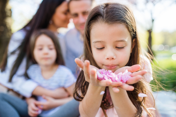 A front view of small girl with family outside in spring nature.