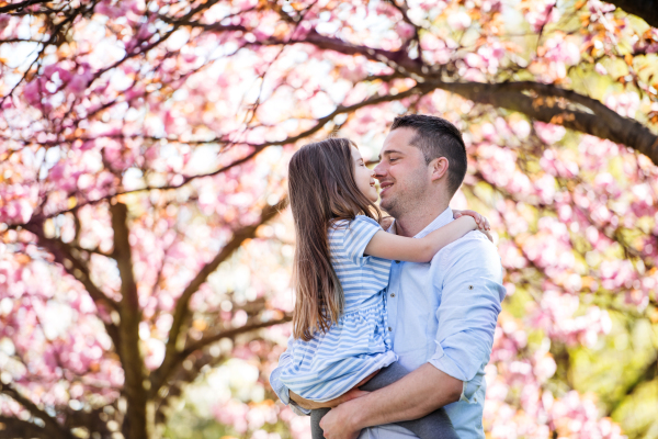 A young father holding small daughter outside in spring nature.