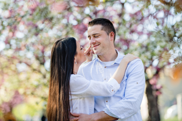 Beautiful young couple in love on a walk outside in spring nature under blossoming trees, hugging.