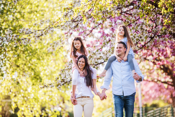 Family of young parents with small daugthers walking outside in spring nature.