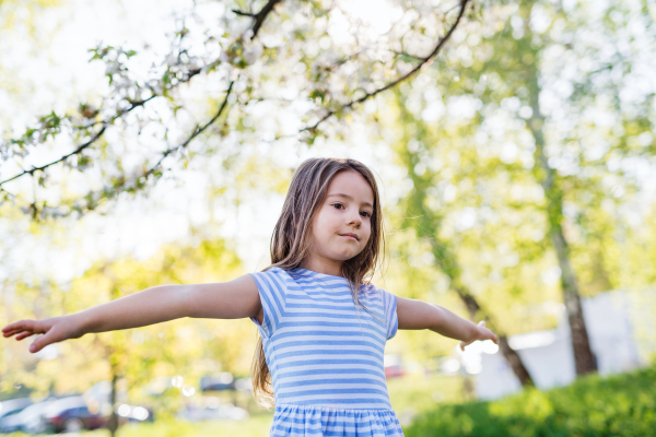 A front view of cheerful small girl playing outside in spring nature.