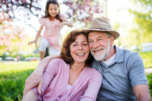 Front view of senior grandparents with small granddaugthers sitting outside in spring nature.