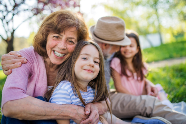 Senior grandparents with granddaughters sitting outside in spring nature, looking at camera.