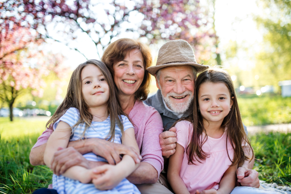 Senior grandparents with granddaughters sitting outside in spring nature, looking at camera.