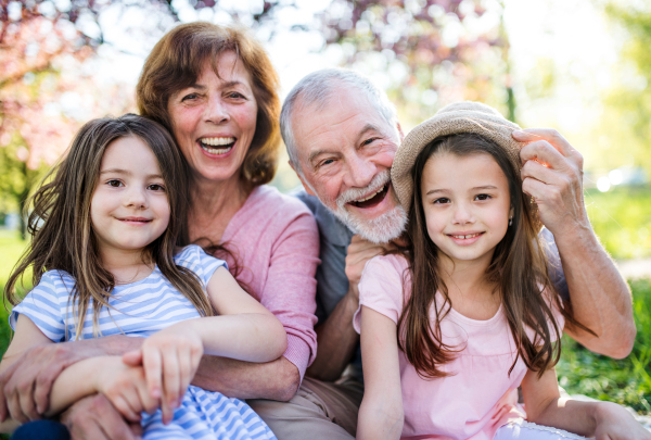 Front view of senior grandparents with small granddaugther sitting outside in spring nature.