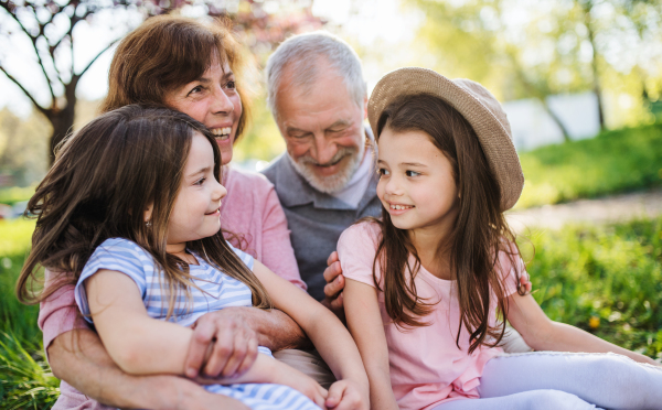 Front view of senior grandparents with small granddaugther sitting outside in spring nature.