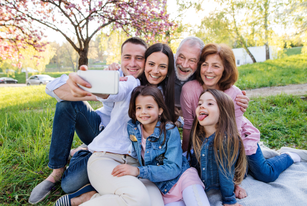 Three generation family with smartphone sitting outside in spring nature, taking selfie.