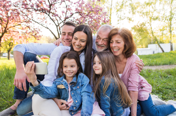 Three generation family with smartphone sitting outside in spring nature, taking selfie.