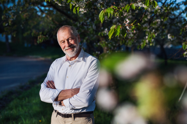 Front view of senior man standing outside in spring nature, looking at camera.