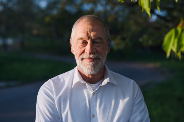 Front view of senior man standing outside in spring nature, eyes closed.