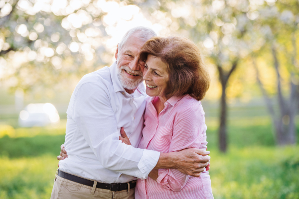 Beautiful senior couple in love on a walk outside in spring nature under blossoming trees, hugging.