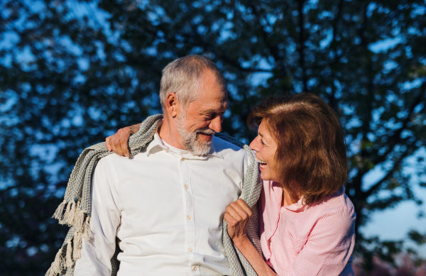 Front view of beautiful senior couple in love outside in spring nature at dusk, talking.