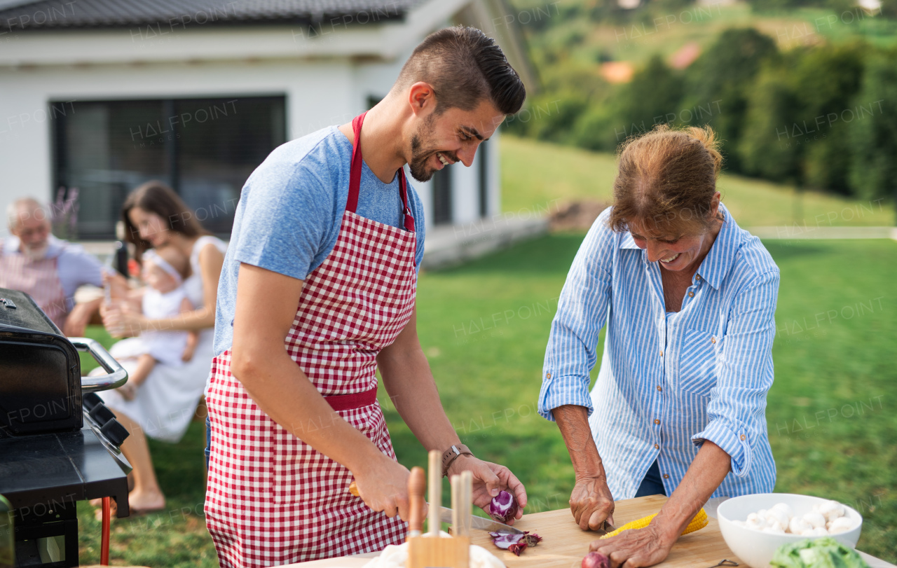 Portrait of multigeneration family outdoors on garden barbecue, grilling and talking.