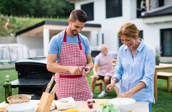 Portrait of multigeneration family outdoors on garden barbecue, grilling and talking.