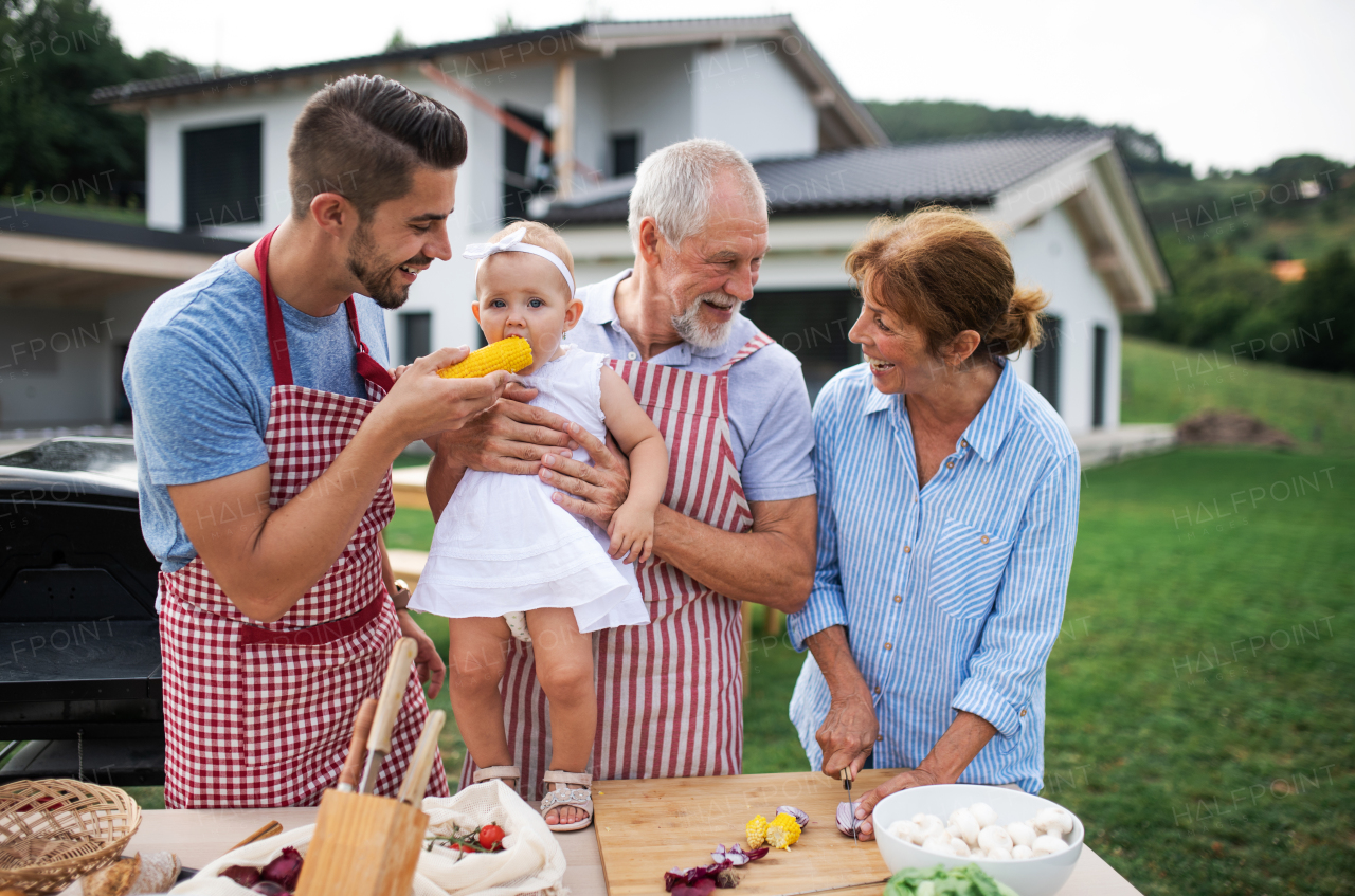 Portrait of multigeneration family outdoors on garden barbecue, grilling and talking.