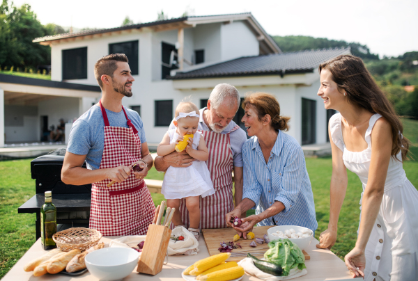 Portrait of multigeneration family outdoors on garden barbecue, grilling and talking.