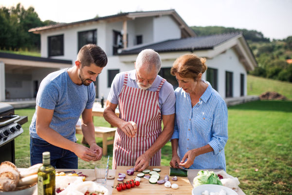 Portrait of multigeneration family outdoors on garden barbecue, grilling and talking.