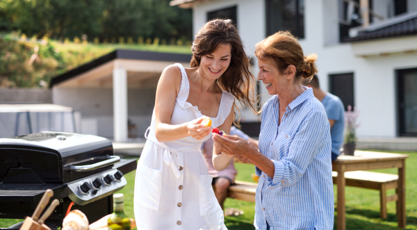 Portrait of multigeneration family outdoors on garden barbecue, grilling and talking.