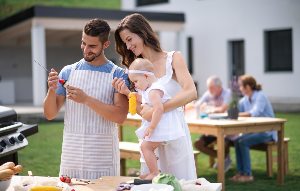 Portrait of happy family with baby outdoors on garden barbecue, grilling.