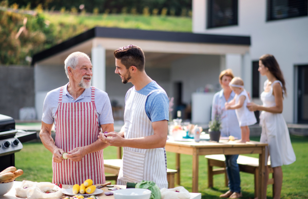 Portrait of multigeneration family outdoors on garden barbecue, grilling and talking.