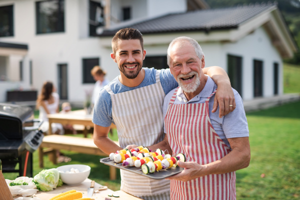 A portrait of father and son outdoors on garden barbecue, grilling.