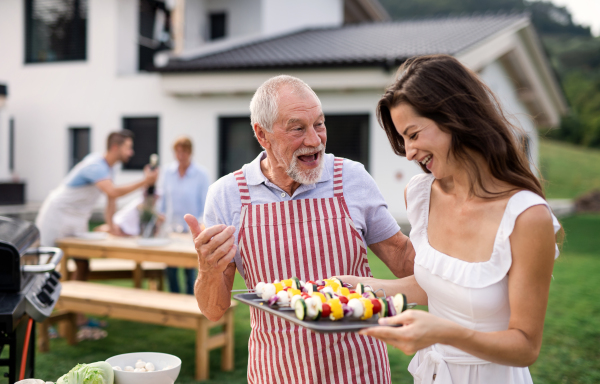 Portrait of multigeneration family outdoors on garden barbecue, grilling and talking.