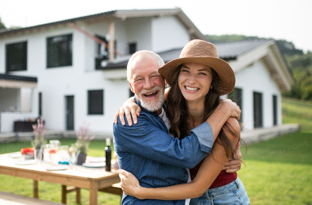 Portrait of senior father with daughter outdoors in backyard, looking at camera.