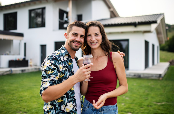 Front view portrait of young couple with wine outdoors in backyard, looking at camera.