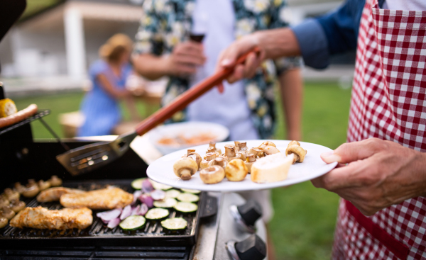 A midsection of family outdoors on garden barbecue, grilling.