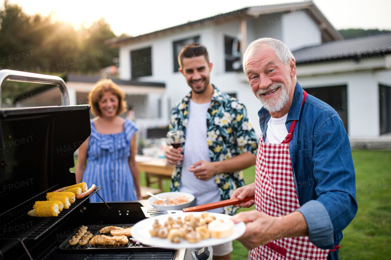 A portrait of multigeneration family outdoors on garden barbecue, grilling.