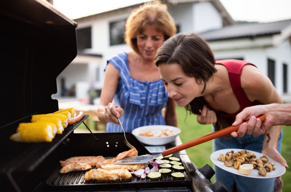 Portrait of multigeneration family outdoors on garden barbecue, grilling and talking.