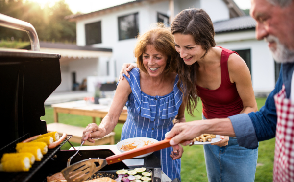 Portrait of multigeneration family outdoors on garden barbecue, grilling and talking.