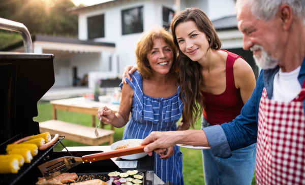 A portrait of multigeneration family outdoors on garden barbecue, grilling.