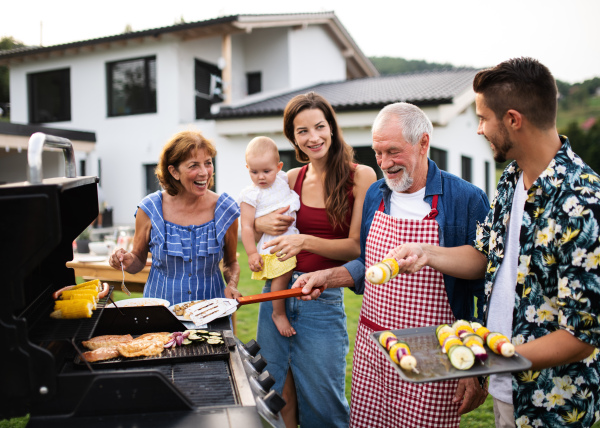 Portrait of multigeneration family outdoors on garden barbecue, grilling and talking.