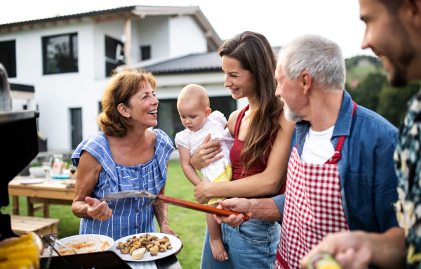 Portrait of multigeneration family outdoors on garden barbecue, grilling and talking.