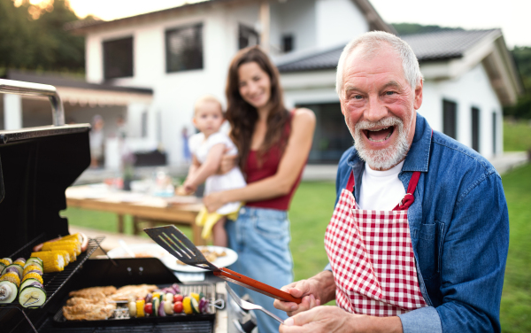 A portrait of multigeneration family outdoors on garden barbecue, grilling.