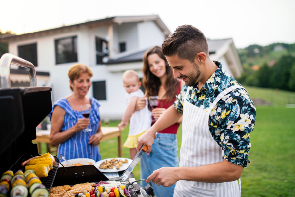 Portrait of multigeneration family outdoors on garden barbecue, grilling and talking.