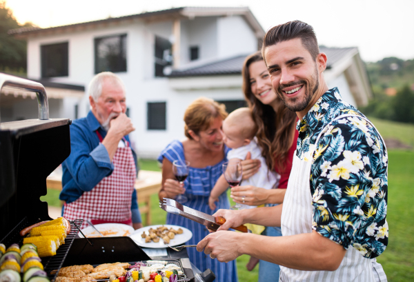 Portrait of multigeneration family outdoors on garden barbecue, grilling and talking.