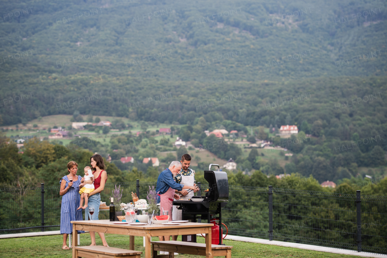 Multigeneration family with wine outdoors on garden barbecue, grilling and talking.