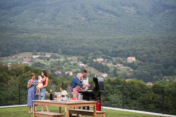 Multigeneration family with wine outdoors on garden barbecue, grilling and talking.