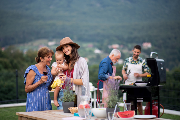 Multigeneration family with wine outdoors on garden barbecue, grilling and talking.