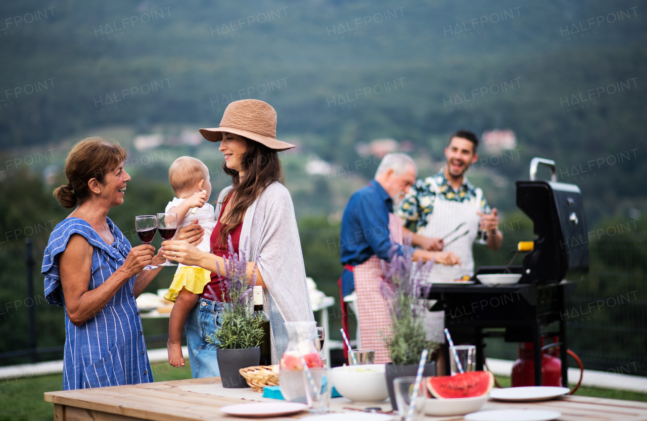 Multigeneration family with wine outdoors on garden barbecue, grilling and talking.