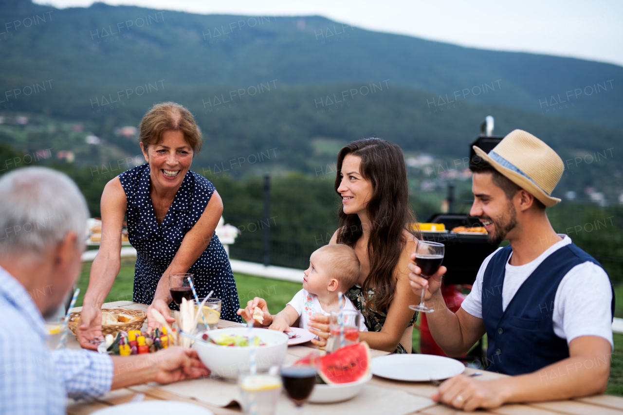 Portrait of multigeneration family sitting at table outdoors on garden barbecue, eating.