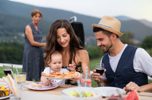 Portrait of family sitting at table outdoors on garden barbecue, eating and drinking wine.