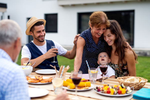 Portrait of multigeneration family sitting at table outdoors on garden barbecue, eating.