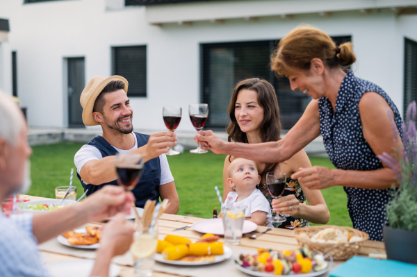 Portrait of family sitting at table outdoors on garden barbecue, eating and drinking wine.