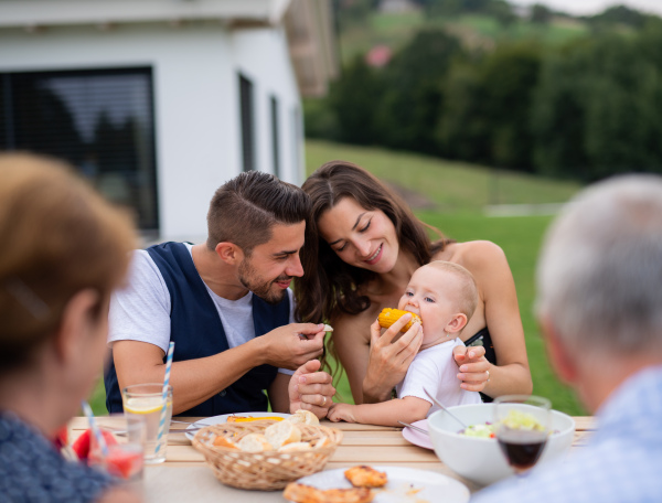 Portrait of multigeneration family sitting at table outdoors on garden barbecue, eating.