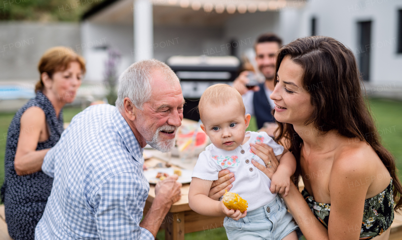 A portrait of extended family sitting at table outdoors on garden barbecue.