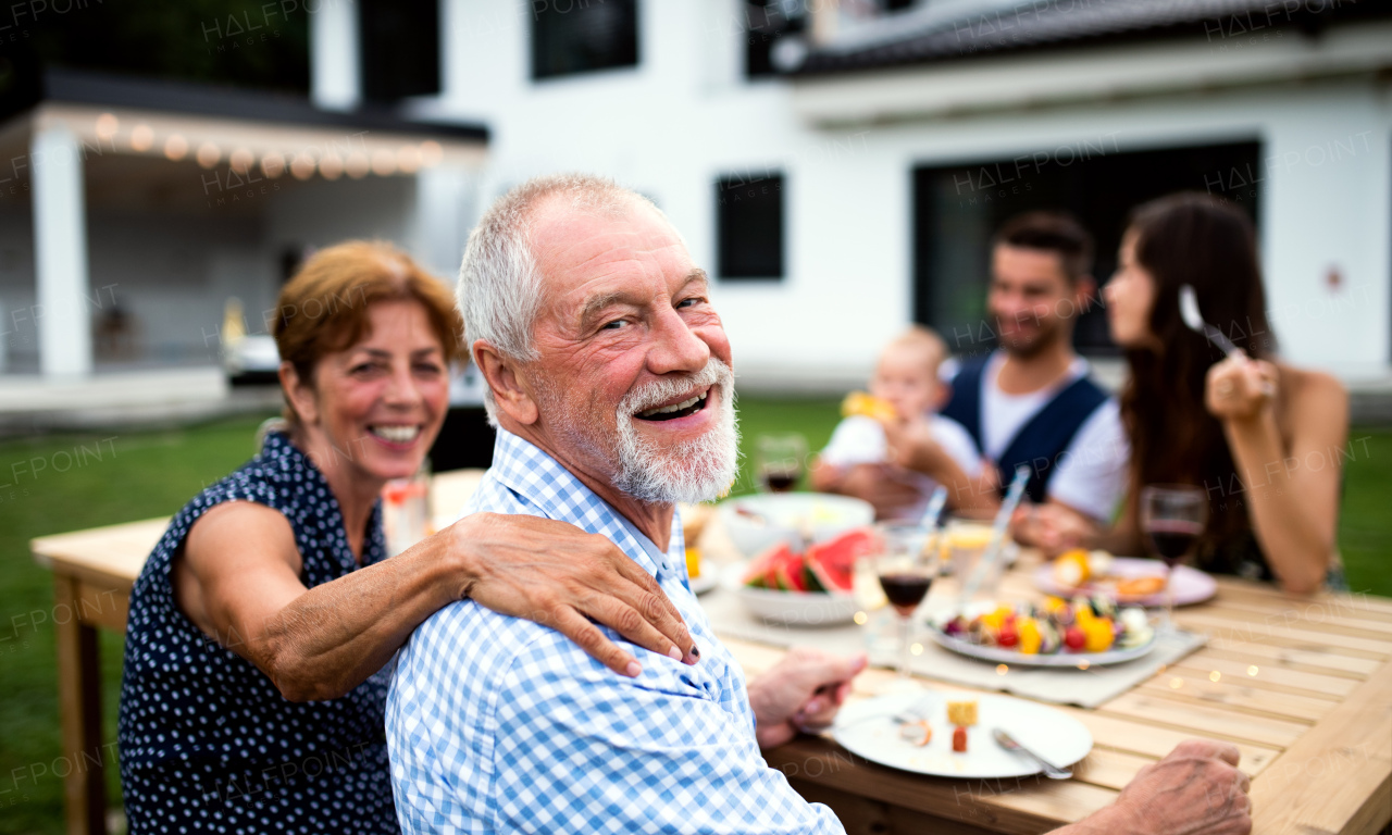 Portrait of multigeneration family sitting at table outdoors on garden barbecue, eating.